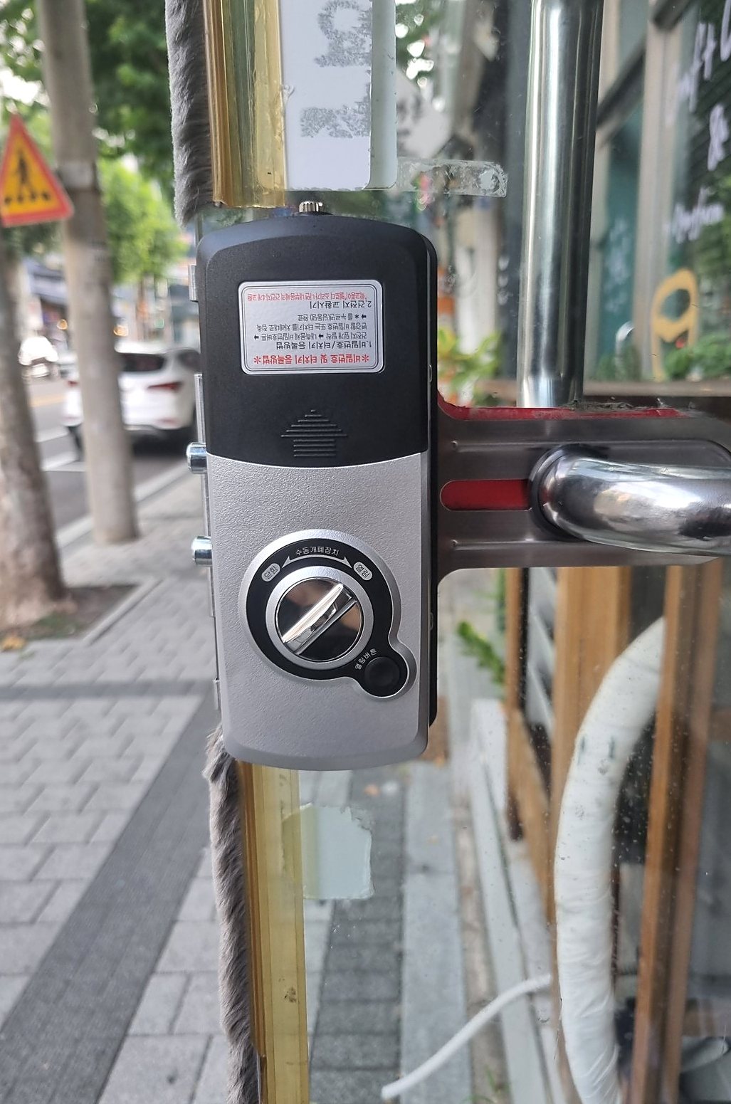안양시 부림동 출장 — 유리문에 단 검은색과 은색 도어락 본체, 옆의 금빛 틀과 회색 털 막이, 스테인리스 손잡이