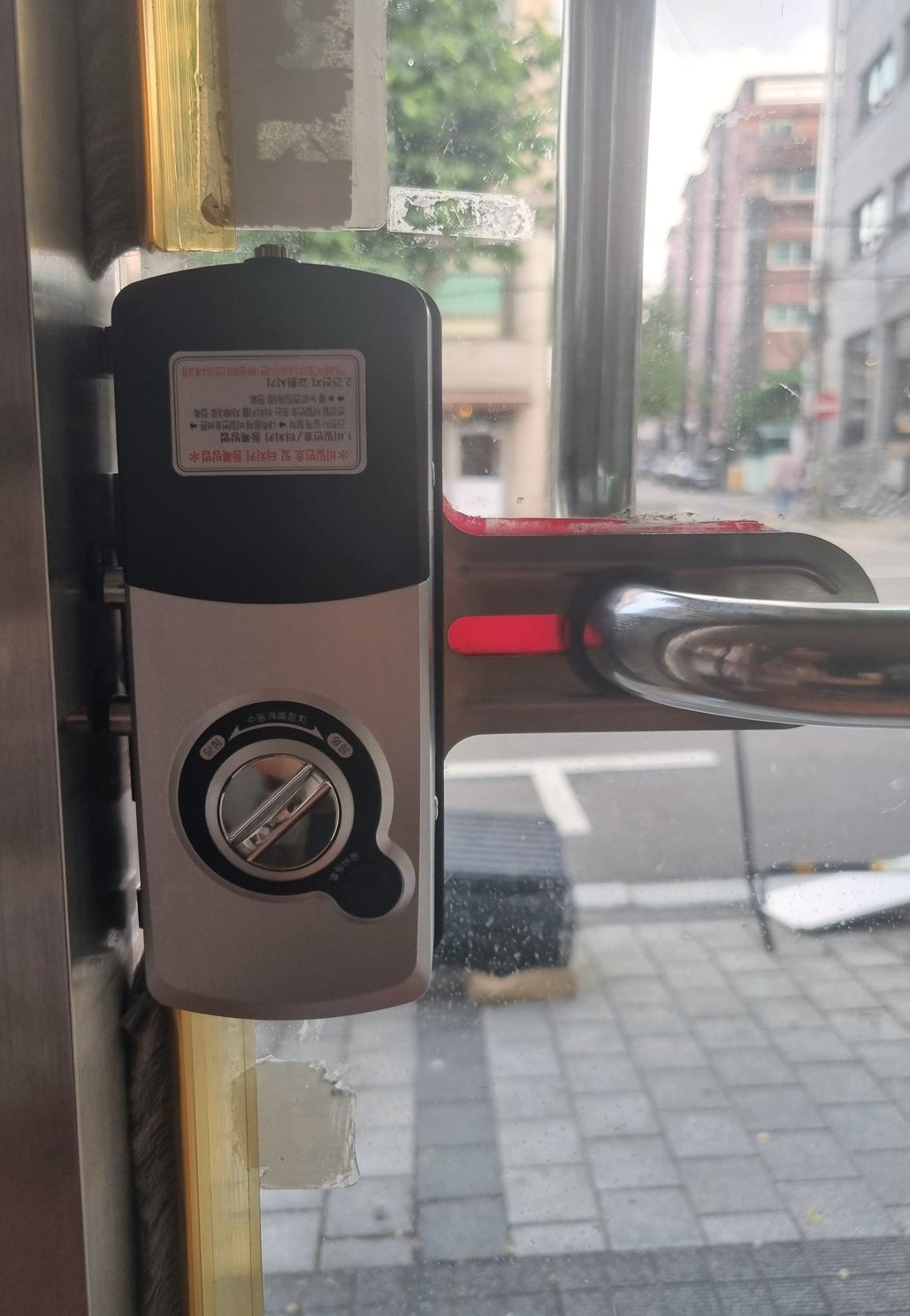 안양시 달안동 출장 — 유리문에 달린 검은 본체 도어락, 아래쪽 둥근 수동 돌림판과 붉은 표시가 있는 손잡이 판