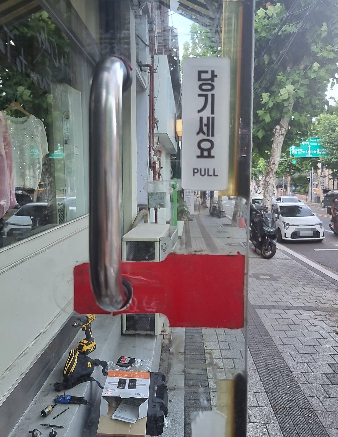 안양시 인덕원동 출장 — 가게 유리문의 은색 당김 손잡이와 문 앞 턱에 놓인 전동 드라이버, 열린 도어락 상자